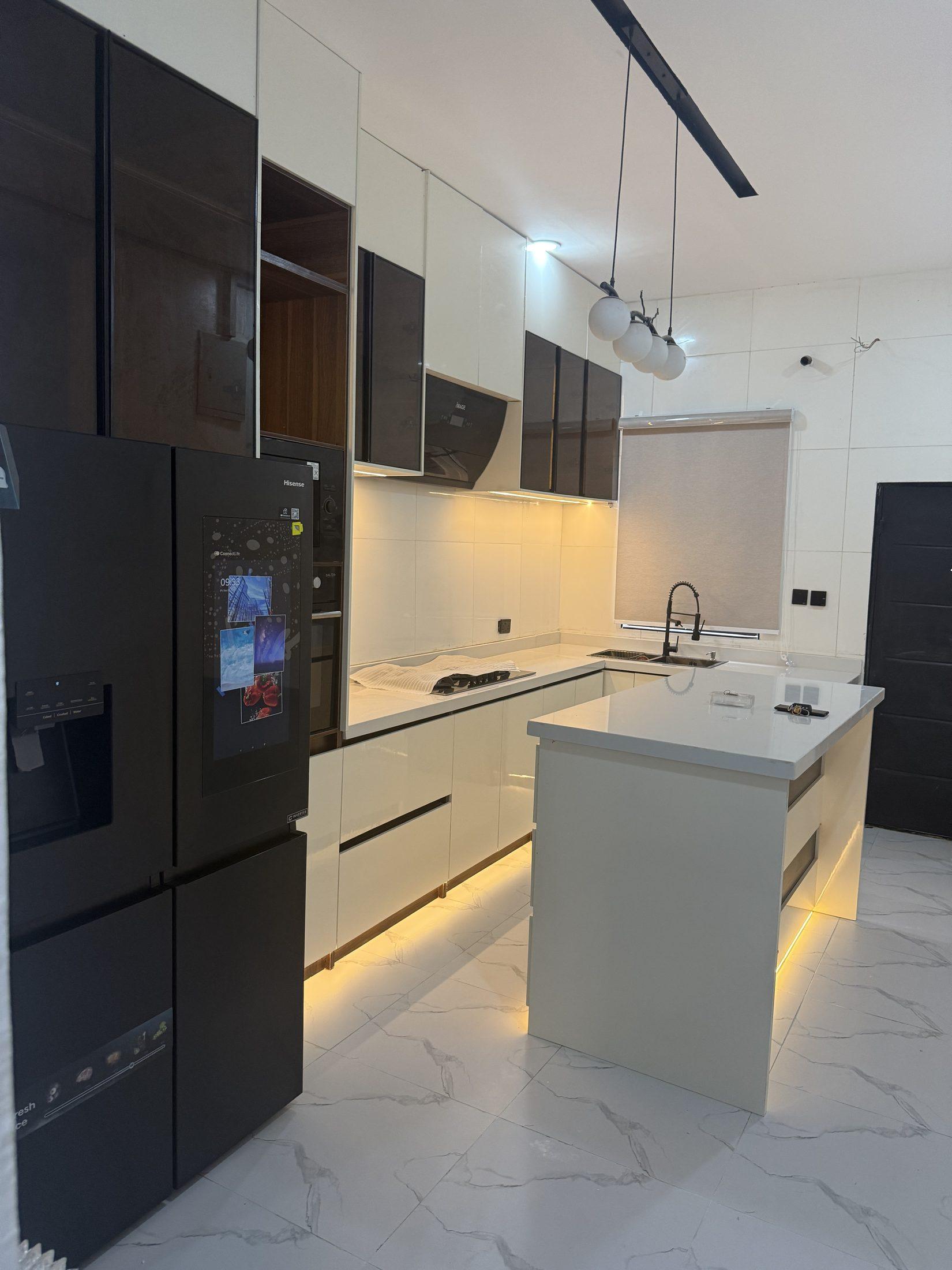 Cream gloss kitchen with smoked glass wall units, a tall appliance wall, globe pendant lights and a lit island